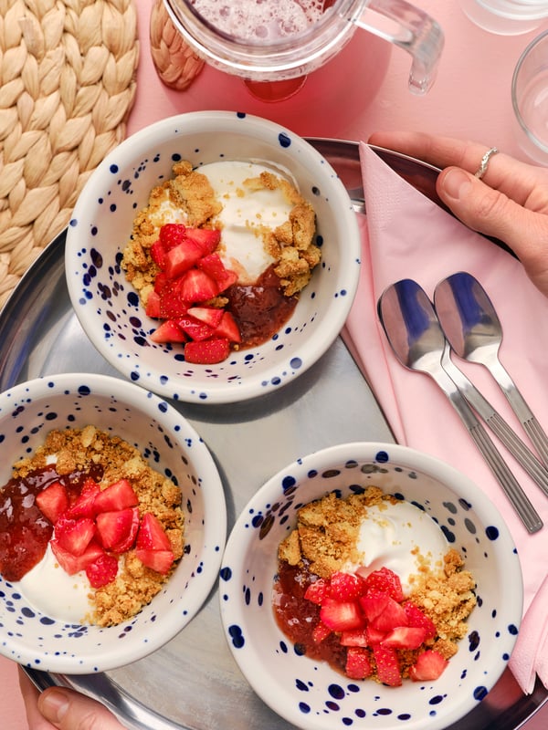 잘게 부순 KAFFEREP 카페레프 비스킷과 딸기, 잼을 곁들인 아침 식사를 담은 그릇 세 개가 올려진 트레이를 들고 있는 사람의 모습.