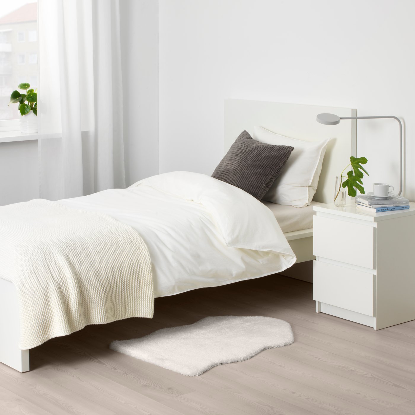TOFTLUND mat on the floor beside a MALM single bed and MALM bedside table in an all-white bedroom.