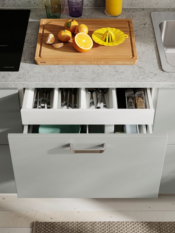 The HAVSTORP light grey kitchen front with a silver handle, with a drawer opened to display cutlery and kitchen tools.