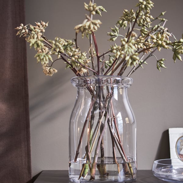 A BEGÄRLIG glass vase of flowers on top of a chest of drawers.