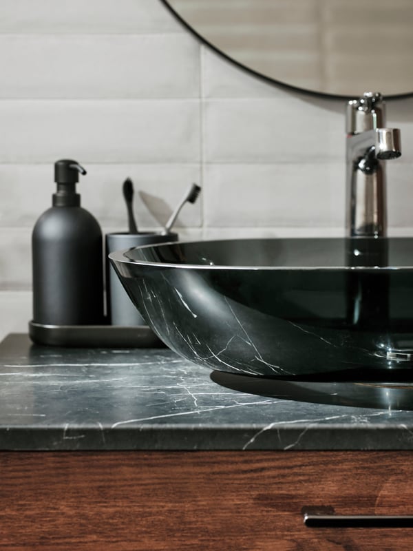 A GODMORGON washstand with two drawers and a TOLKEN countertop with an OXMYREN countertop washbasin in dark grey glass.