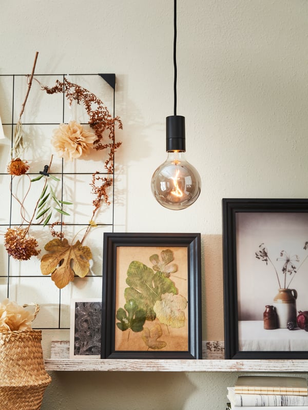 IKEA MOLNART LED light bulb hanging from a black pendant light cord above an EDSBRUK and BILD picture frames on a shelf