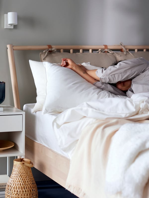 Osoba s nataženýma rukama leží v posteli, kde jsou vidět výrobky IKEA.