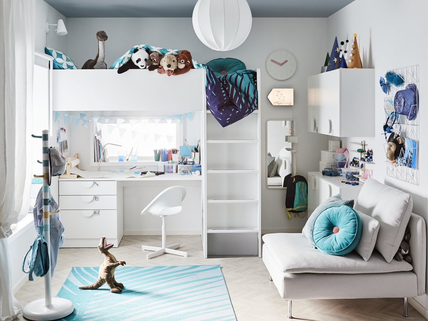 Helles Kinderzimmer mit Hochbett und integriertem Schreibtisch, weißen Möbeln und viel Stauraum. Raum in Blau- und Weißtönen mit Teppich, Sofa, dekorativen Kissen und Spielzeug – ideal für funktionales und gemütliches Wohnen.