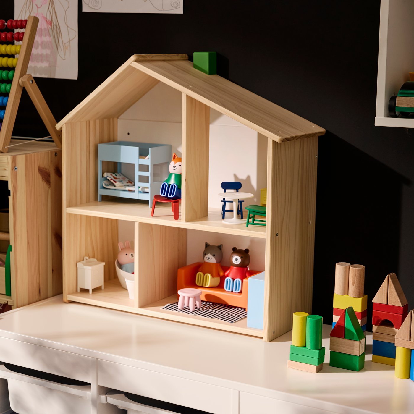 FLISAT doll’s house standing on TROFAST storage unit, with the house furnished with HUSET doll’s figures and furniture.