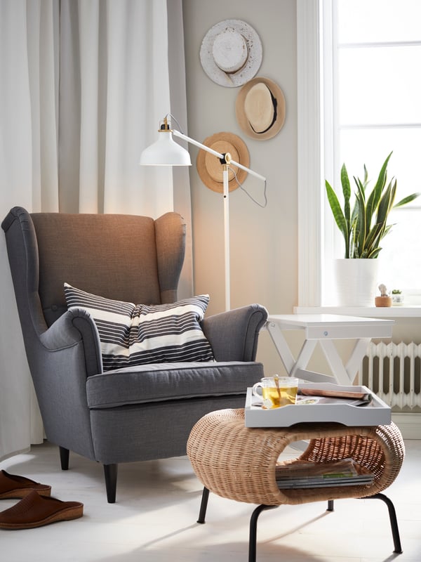 An IKEA STRANDMON dark grey wing chair in the corner of a living space, with a rattan coffee table and tray.