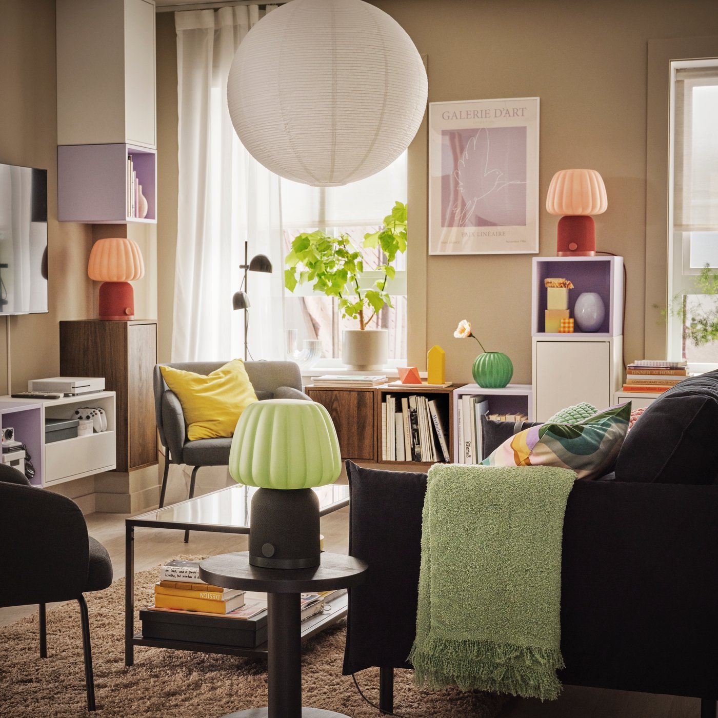 Un soggiorno luminoso e colorato, con piante, oggetti decorativi e tre lampade/casse Bluetooth KULGLASS in vari punti della stanza.