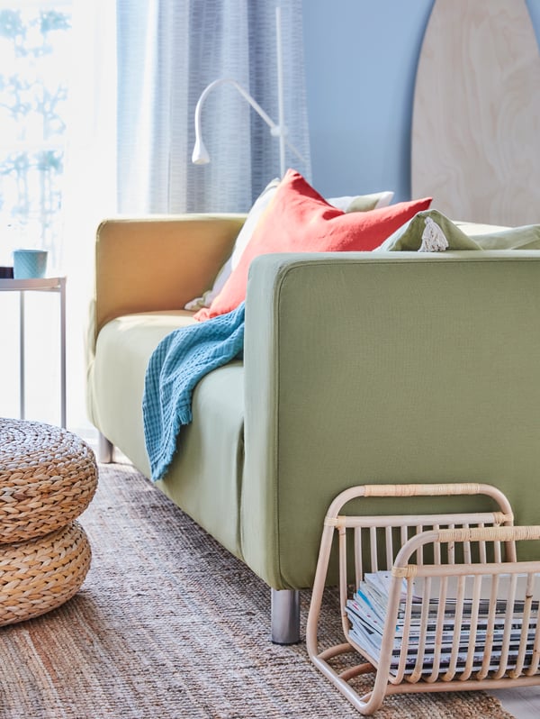 A yellow-green sofa, rust and green-striped cushions, dark blue throw, woven rug, bamboo magazine holder, white floor lamp.