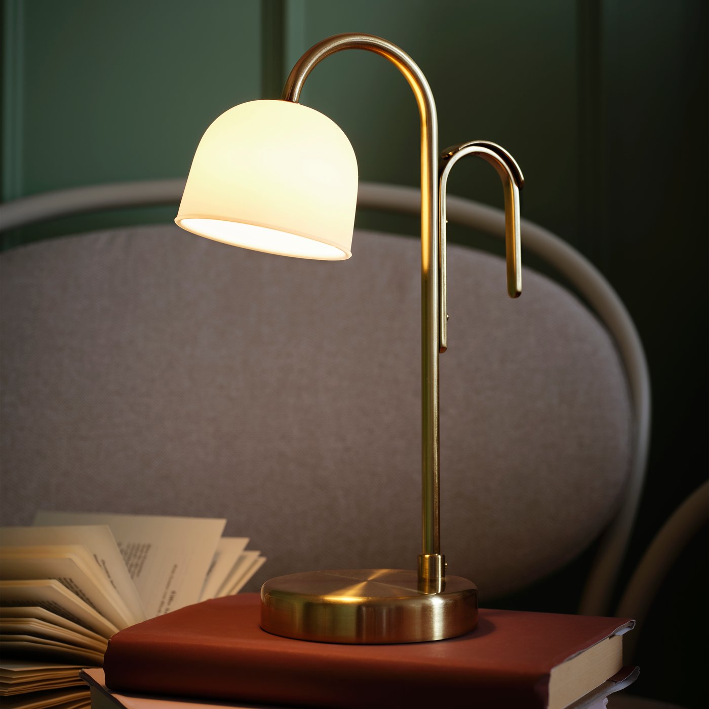 Una lampada portatile a LED TVÅMASTAD bianco opalino in cima a una pila di libri appoggiati su una comoda poltrona.