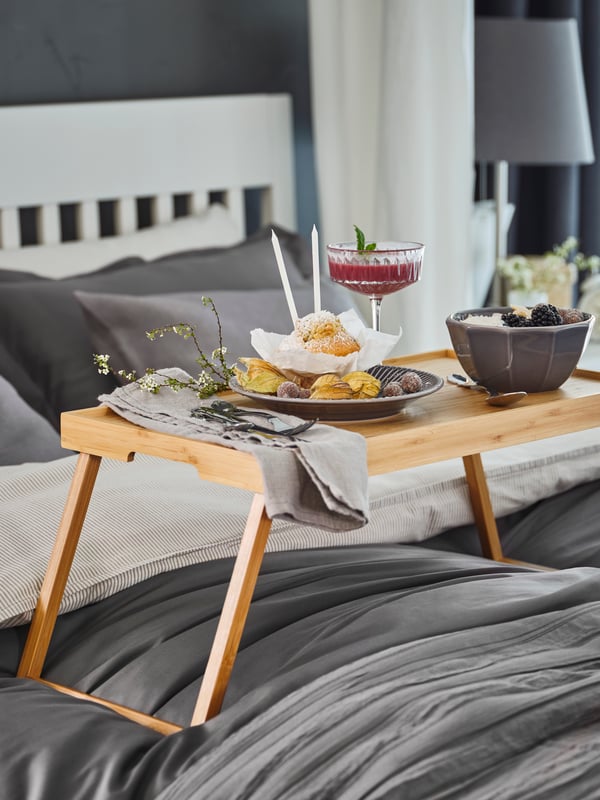 A bamboo RESGODS bed tray with a luxurious breakfast stands on an IDANÄS bed with white and grey bed textile products.