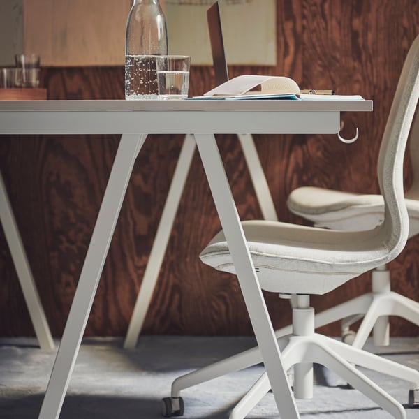Chaise de bureau HATTEFJÄLL beige devant un bureau TROTTEN blanc sur lequel sont posés une bouteille d’eau, un verre et un bloc-notes.