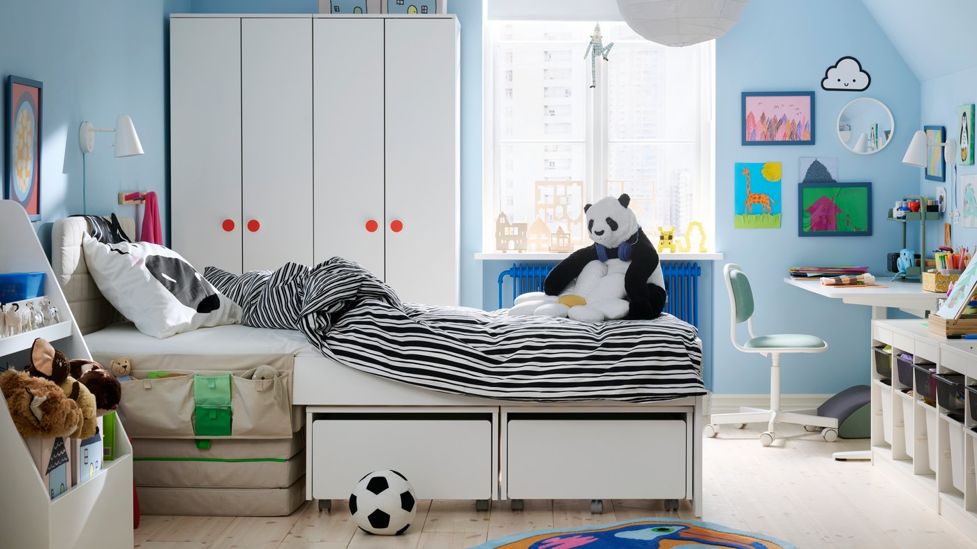 Chambre d’enfant avec lit SLÄKT agrémenté de linge de lit NATTHÄGER au milieu. Armoires et fenêtre à l’arrière-plan.