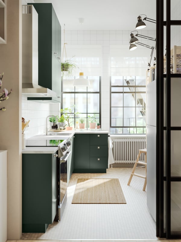 A kitchen with deep green kitchen fronts, a white marble effect/laminate EKBACKEN countertop and a white/birch pendant lamp.