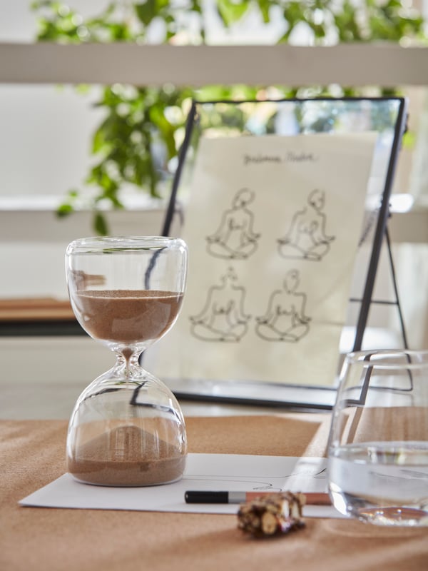 Artículos decorativos sobre una mesa. En primer plano un reloj de arena y detrs un marco de vidrio para mesa.