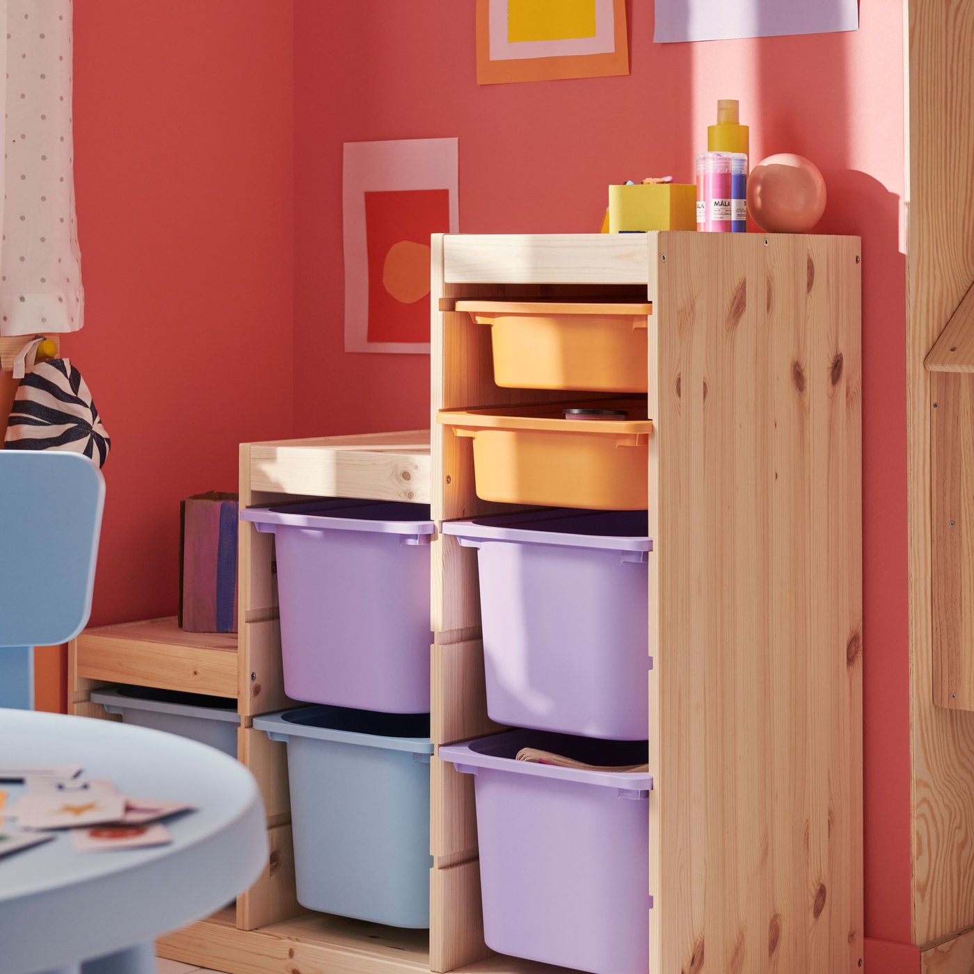 A light white stained pine TROFAST frame holding storage boxes in lilac, light blue and light orange in a children’s room.