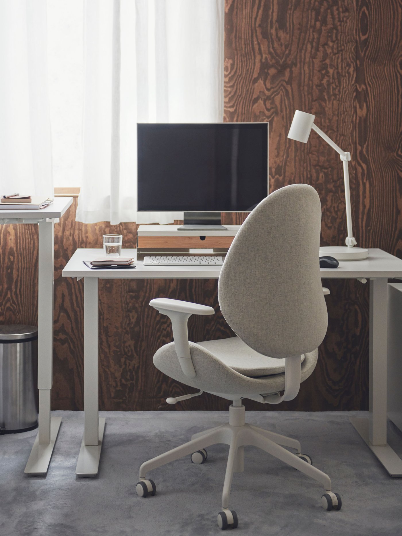 Un estudio con un escritorio de altura ajustable y una silla de escritorio HATTEFJÄLL con ruedas y apoyabrazos.