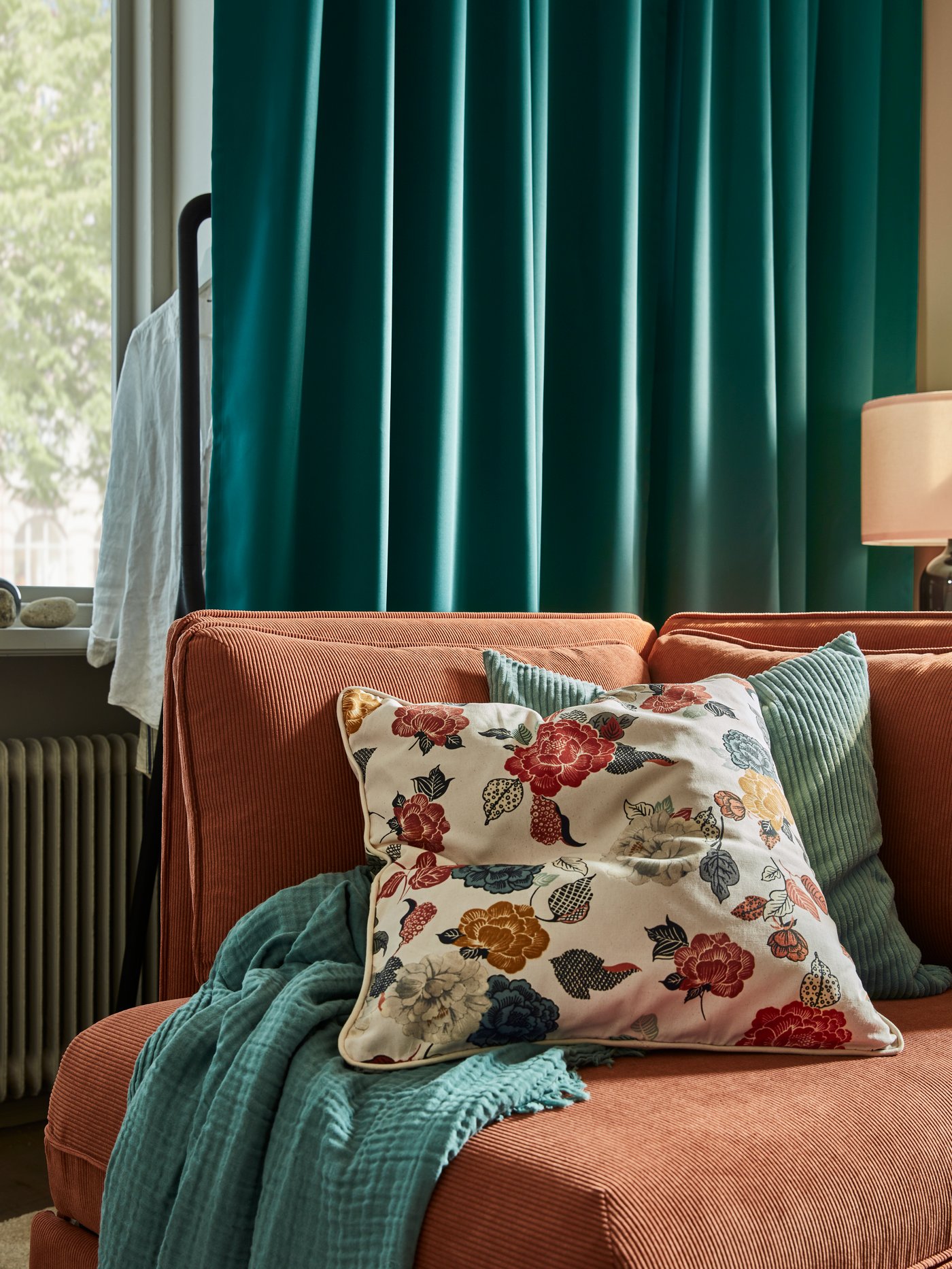 Cushions in a grey-turquoise ÅSVEIG cover and a natural/flower patterned TROLLMALL cover sit on a VALLENTUNA sofa-bed module.