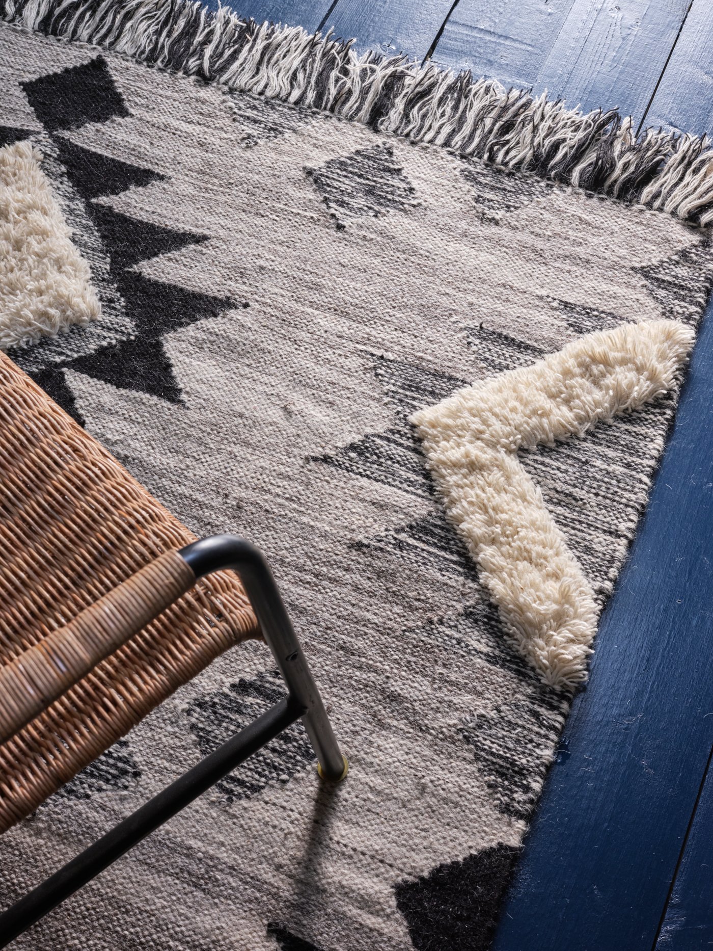 Alfombra TANNISBY color gris con diseños geométricos. Se ve sobre ésta una silla de material tipo mimbre o ratán.