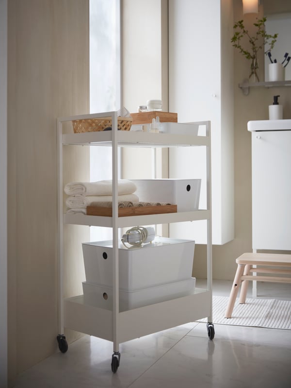 White NISSAFORS trolley with different sizes of KUGGIS secondary storage boxes on each level, and other toiletry items organised neatly on top.