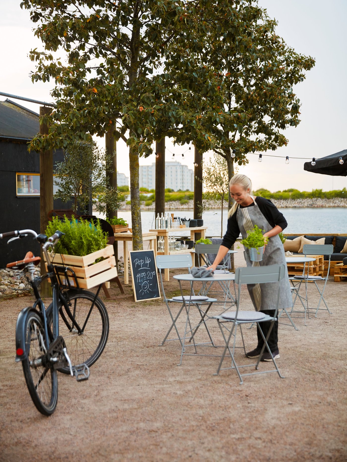A person cleans a grey SUNDSÖ table on a patio with a cleaning cloth.