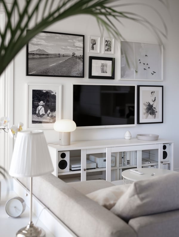 TV lekap dinding digantung di samping karya seni berbingkai pada kabinet TV HAVSTA berwarna putih bertentangan katil sofa FRIHETEN berwarna kuning air di ruang tamu.