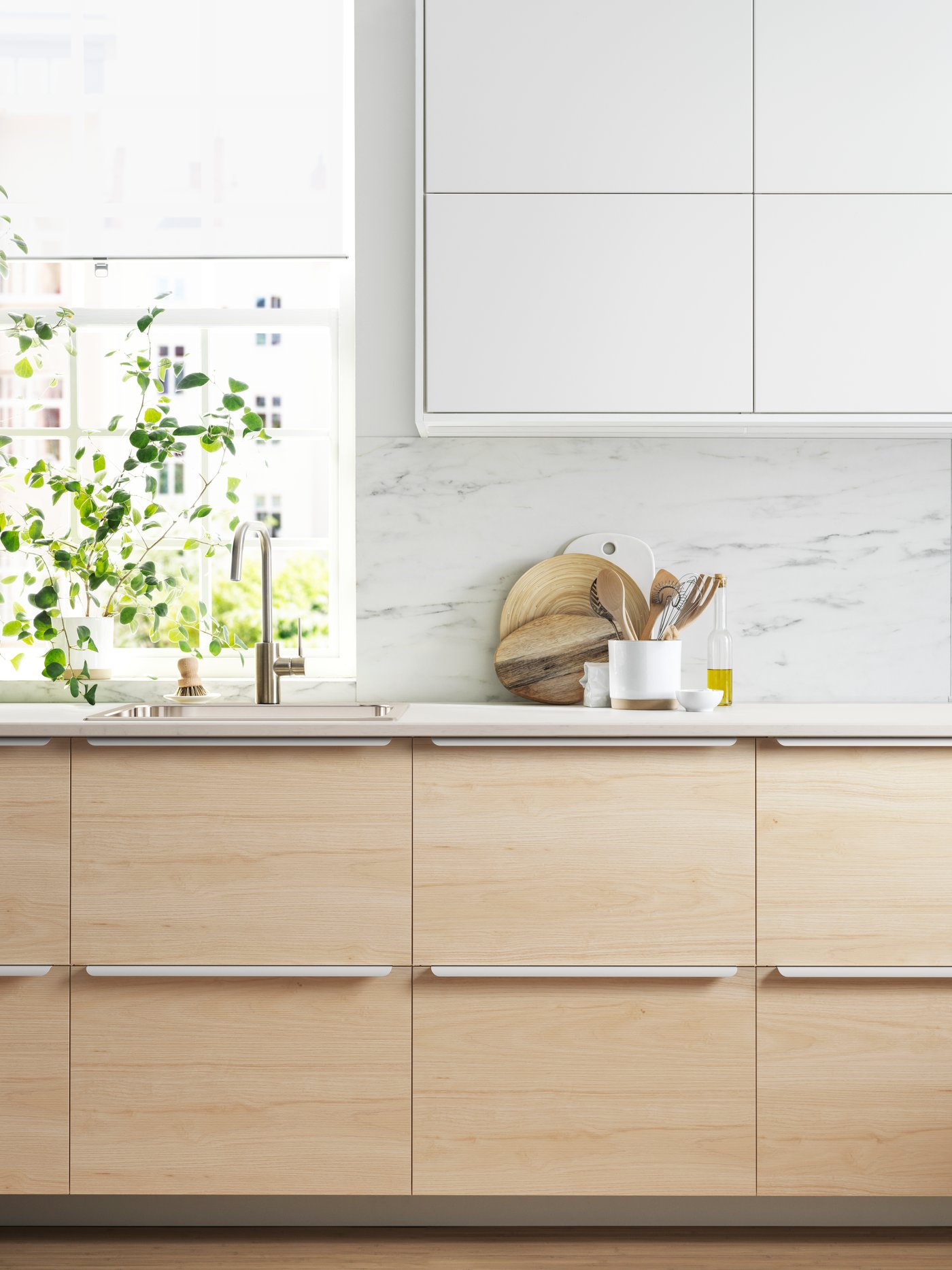 Vista frontal de una cocina con muebles METOD de piso y muralla. Sobre la cubierta de cocna hay unas plantas y una tabla de madera.