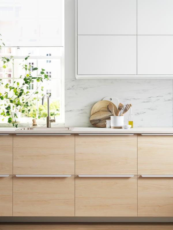 Vista frontal de una cocina con muebles METOD de piso y muralla. Sobre la cubierta de cocna hay unas plantas y una tabla de madera.