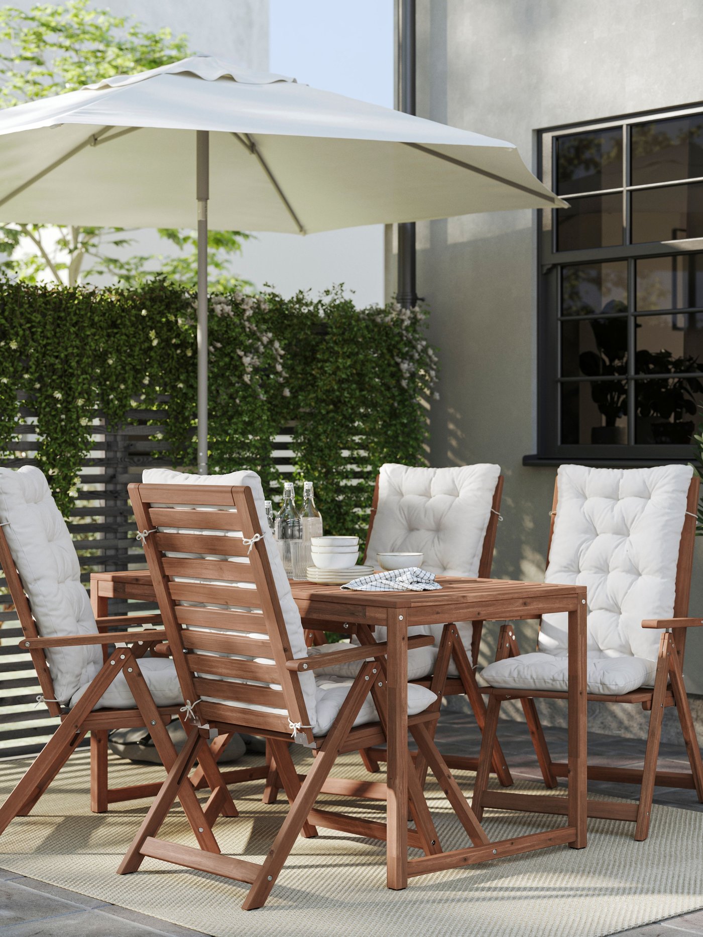 Un comedor de terraza NÄMMARÖ con sillas reclinables de madera tapado con un quitasol blanco.