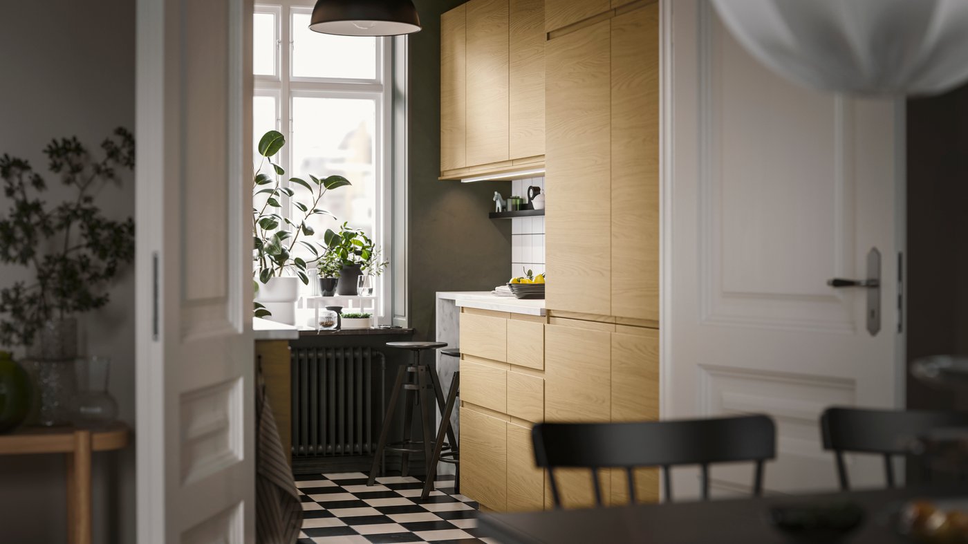 A small and streamlined kitchen has VOXTORP fronts in oak effect with integrated handles and a black SKURUP pendant lamp.