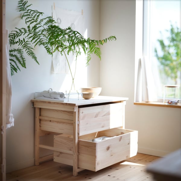 KRONÖREN chest of 2 drawers in pine with plant and bowl on top placed beside a window in a bright bedroom.