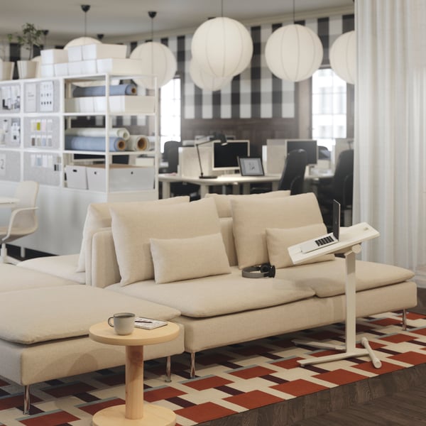 Canapé SÖDERHAMN beige avec pieds en métal, couplé à une table pour ordinateur portable MITTZON, le tout placé sur un tapis à motifs géométriques.