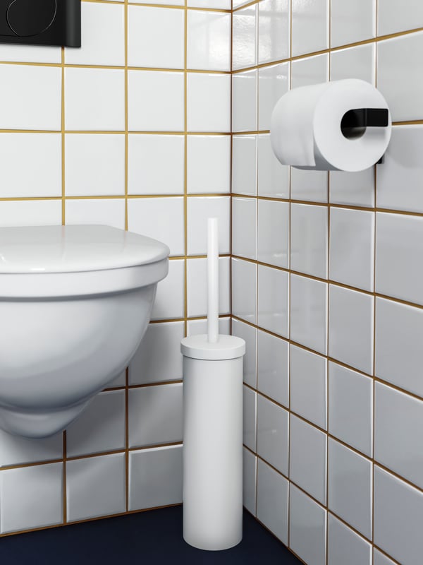 A white toilet brush holder beside the toilet bowl, black toilet roll holder, white tiles with yellow grout.