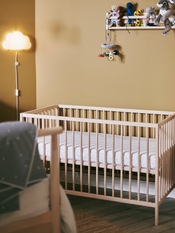 A SNIGLAR cot in a bedroom corner with FLISAT wall storage on one wall and an UPPLYST cloud shape LED wall lamp on the other.