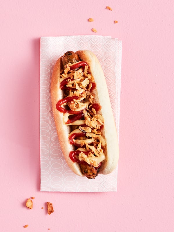 A KORVMOJ vegetable hot dog with ROSTAD LÖK fried onions on a KORVBRÖD hot dog bread, served on a paper napkin.