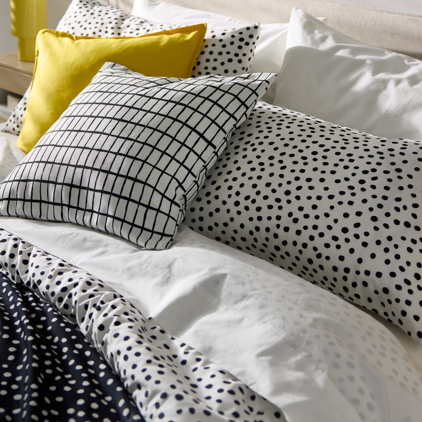 Black and white dot-themed bedding and a yellow cushion.