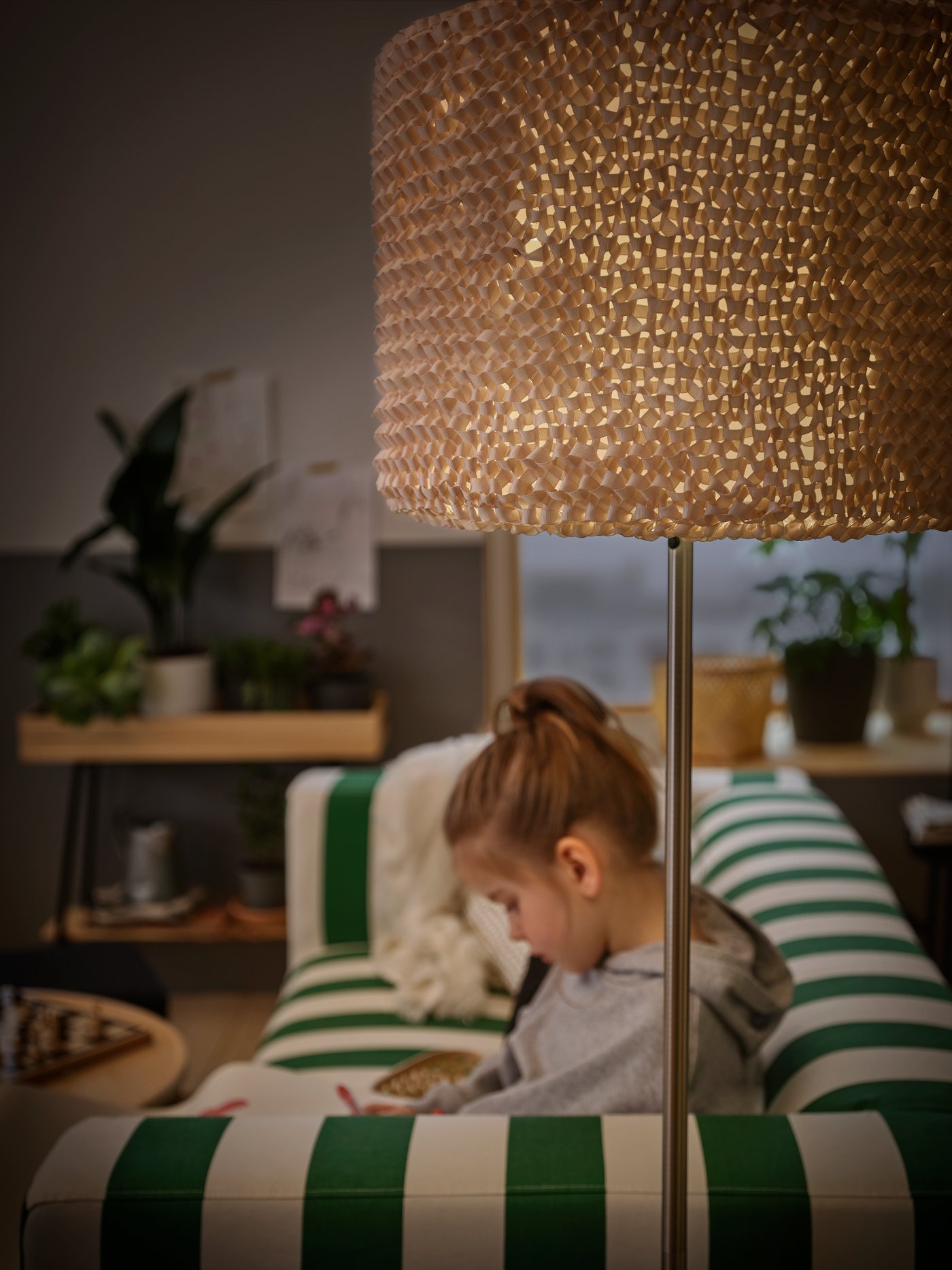A little girl on a KLIPPAN sofa focuses on a drawing. A SKAFTET floor lamp base with LERGRYN lamp shade is beside the sofa.