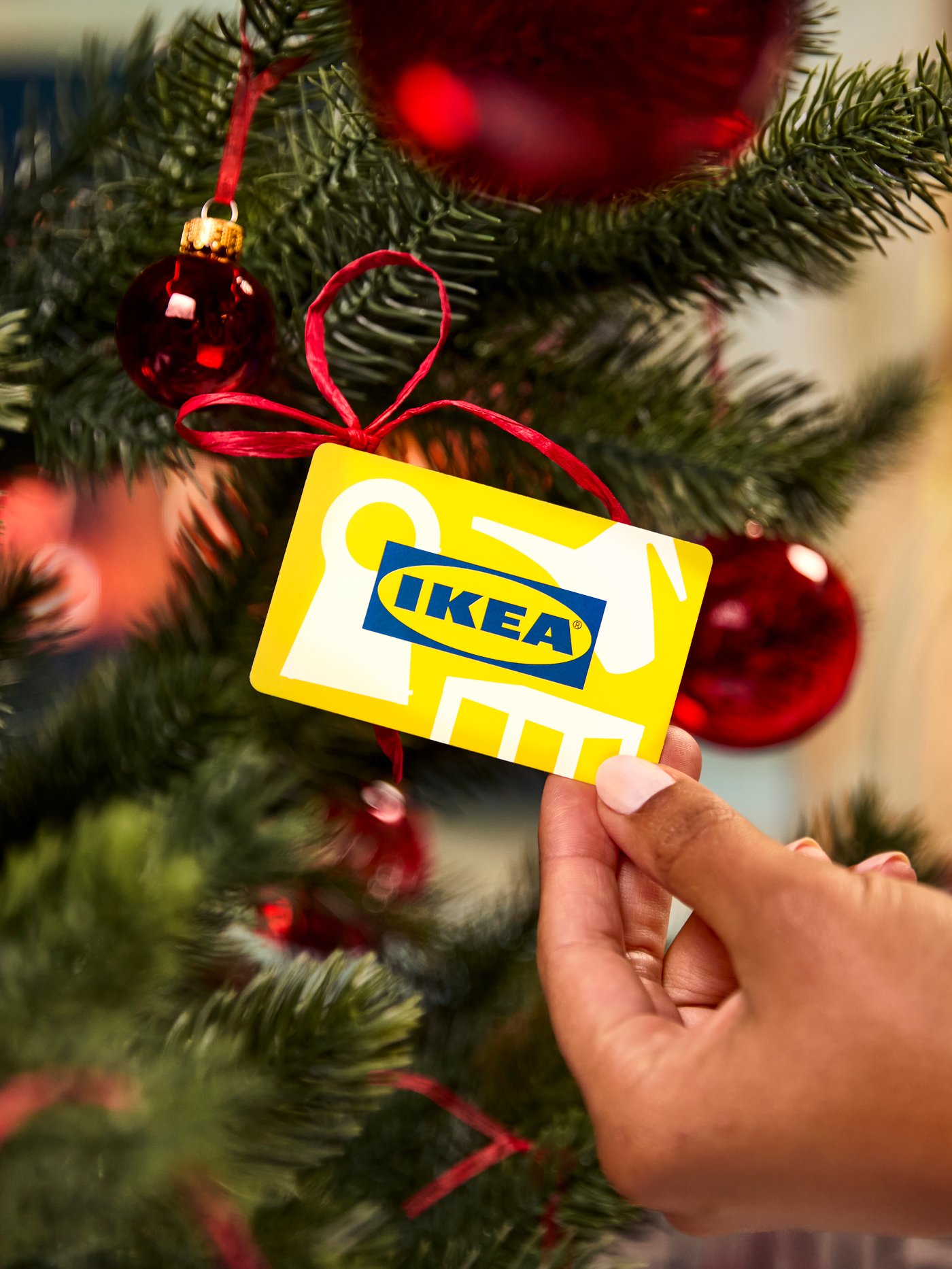 Osoba drži IKEA poklon-karticu koja visi na novogodišnjoj jelci.