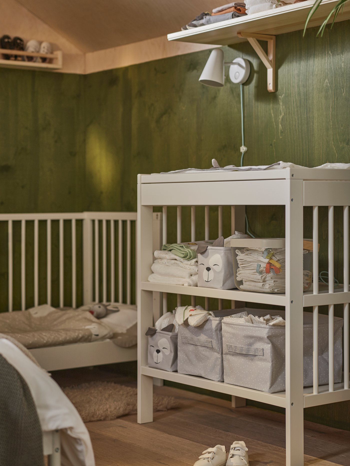 A white GULLIVER changing table holding DRÖMSLOTT storage boxes and accessories beside a GULLIVER cot with one side removed.