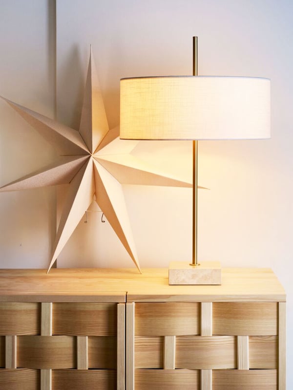 Noventinspiration i form av ett skåp med en vit bordslampa och en vit adventsstjärna lutad mot väggen.