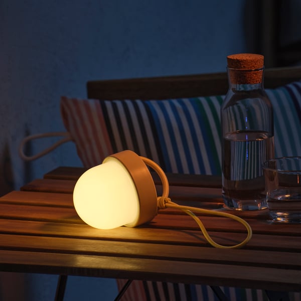A beige battery-operated SOLVINDEN LED pendant lamp in the shape of a globe, illuminating a balcony table.