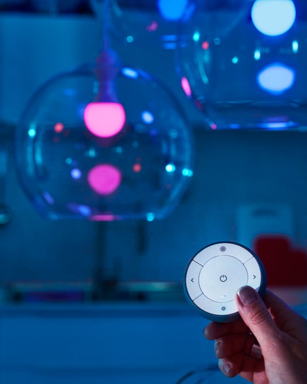 A hand controlling JAKOBSBYN pendant lampshades in glass with dimmable TRÅDFRI LED bulbs with a TRÅDFRI remote control.