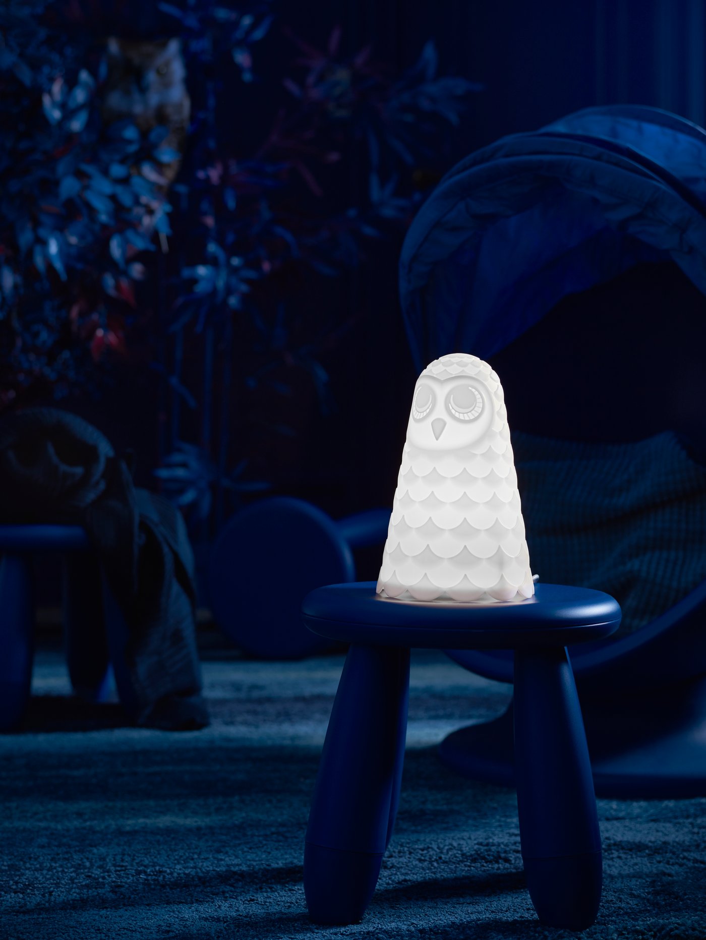 A lit SOLBO LED table lamp sits on a MAMMUT stool in the dark in the middle of the floor in a child’s room.