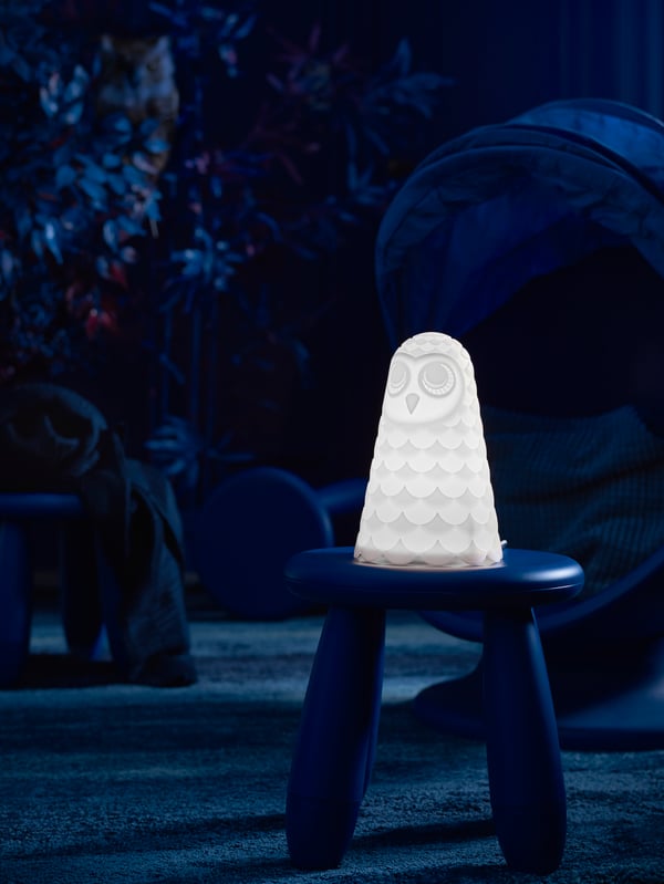Una lámpara de mesa LED SOLBO prendida apoyada en un piso MAMMUT en la oscuridad, en medio de un dormitorio de niños.