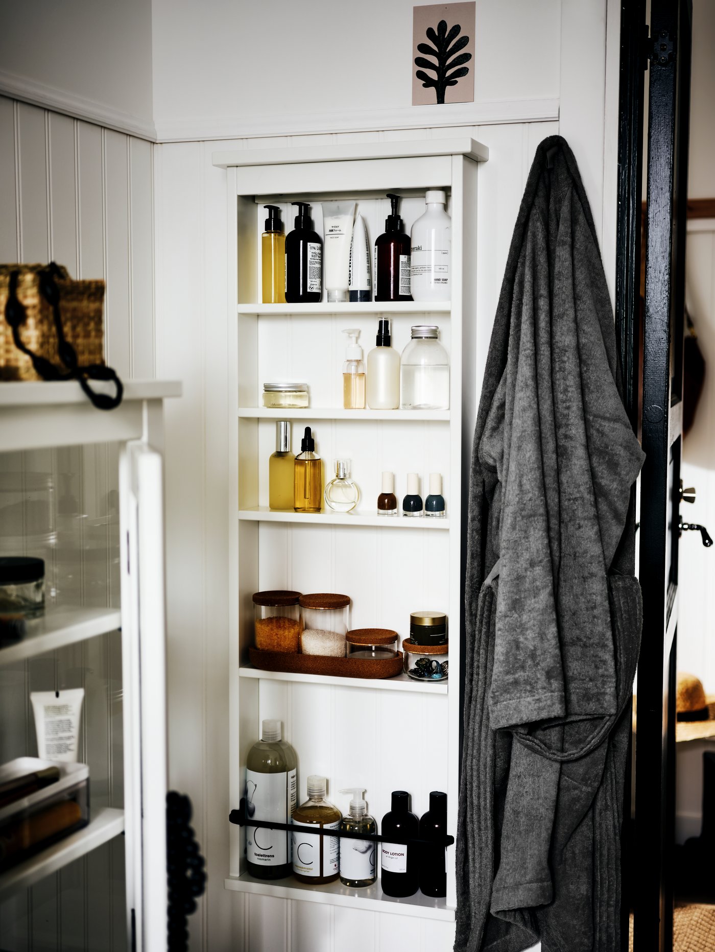 The corner of a white bathroom with a HEMNES wall shelf on one wall. Toiletries and bathroom accessories are on the shelves.