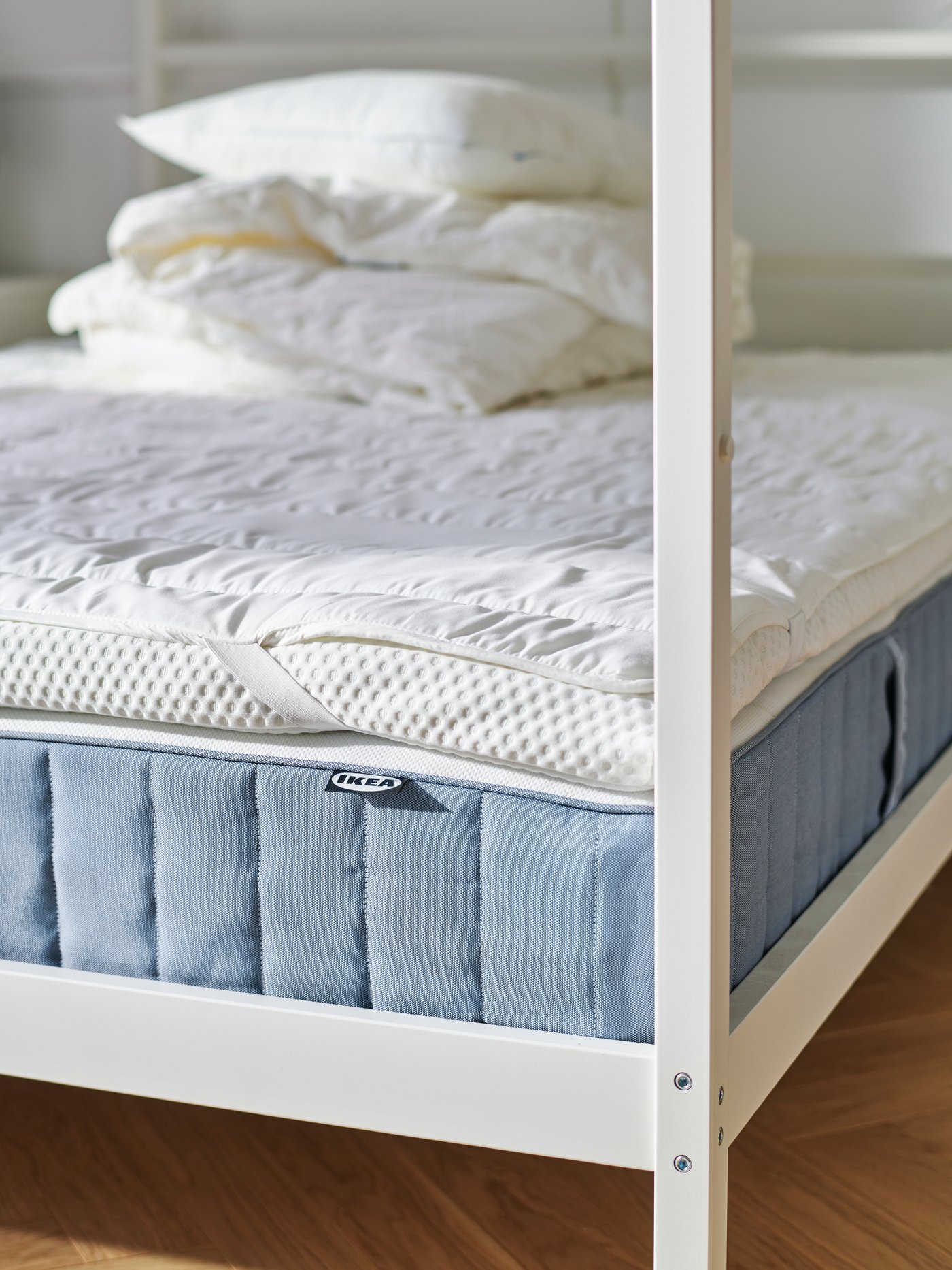 VITARNA four-poster bed with the different layers of mattresses visible, and a pile of duvets and pillows on top of it all.
