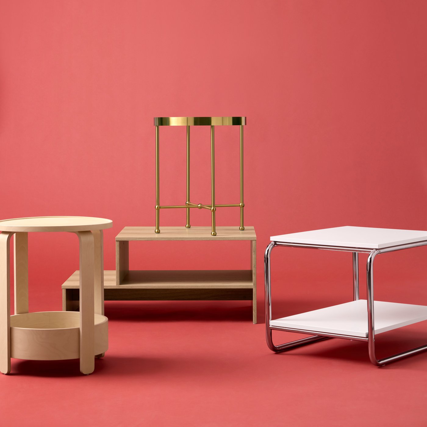 An arrangement of four small tables, one of them a TORSJÖ gold-effect side table, placed against an orange-red background.