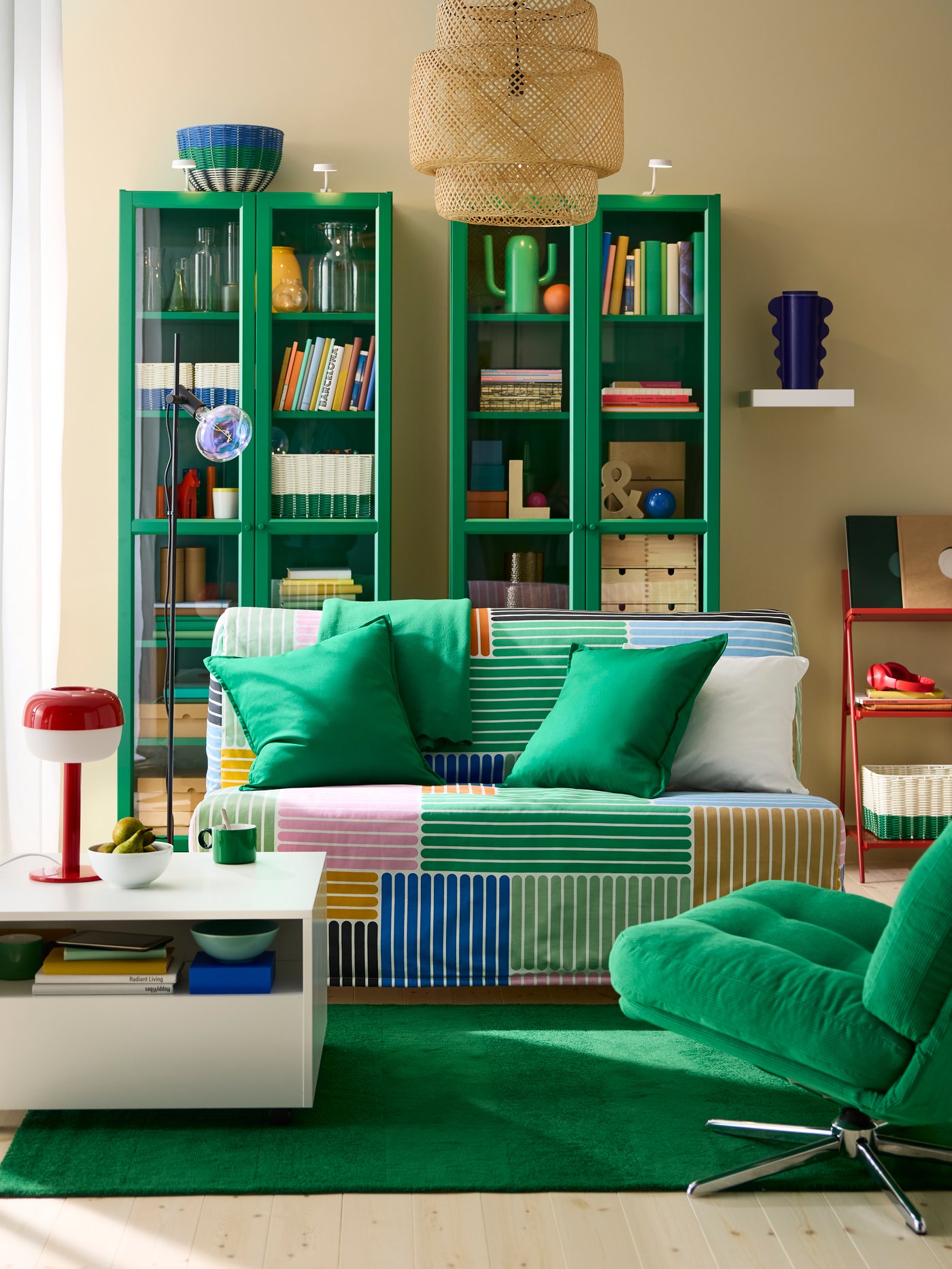 Living room with two green glass display cabinets side by side, small sofa-bed with multi-coloured cover and green rug.
