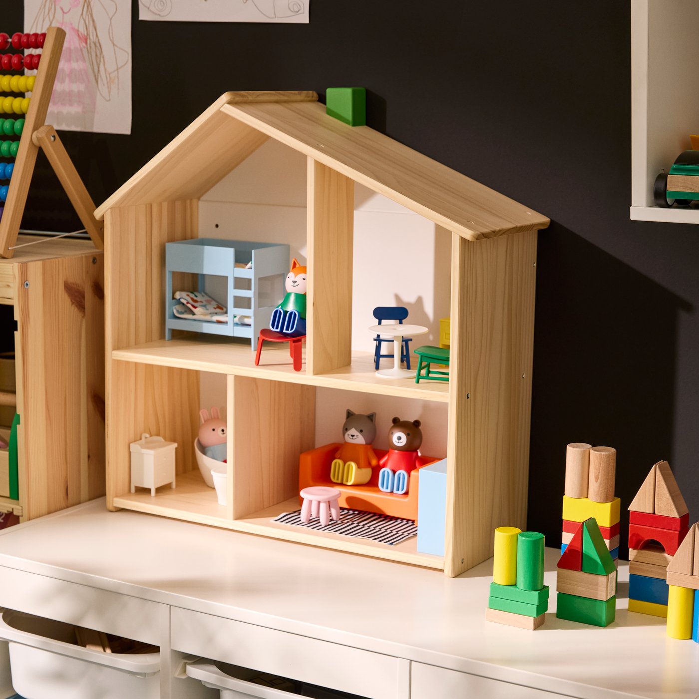 FLISAT doll’s house standing on TROFAST storage unit, with the house furnished with HUSET doll’s figures and furniture.