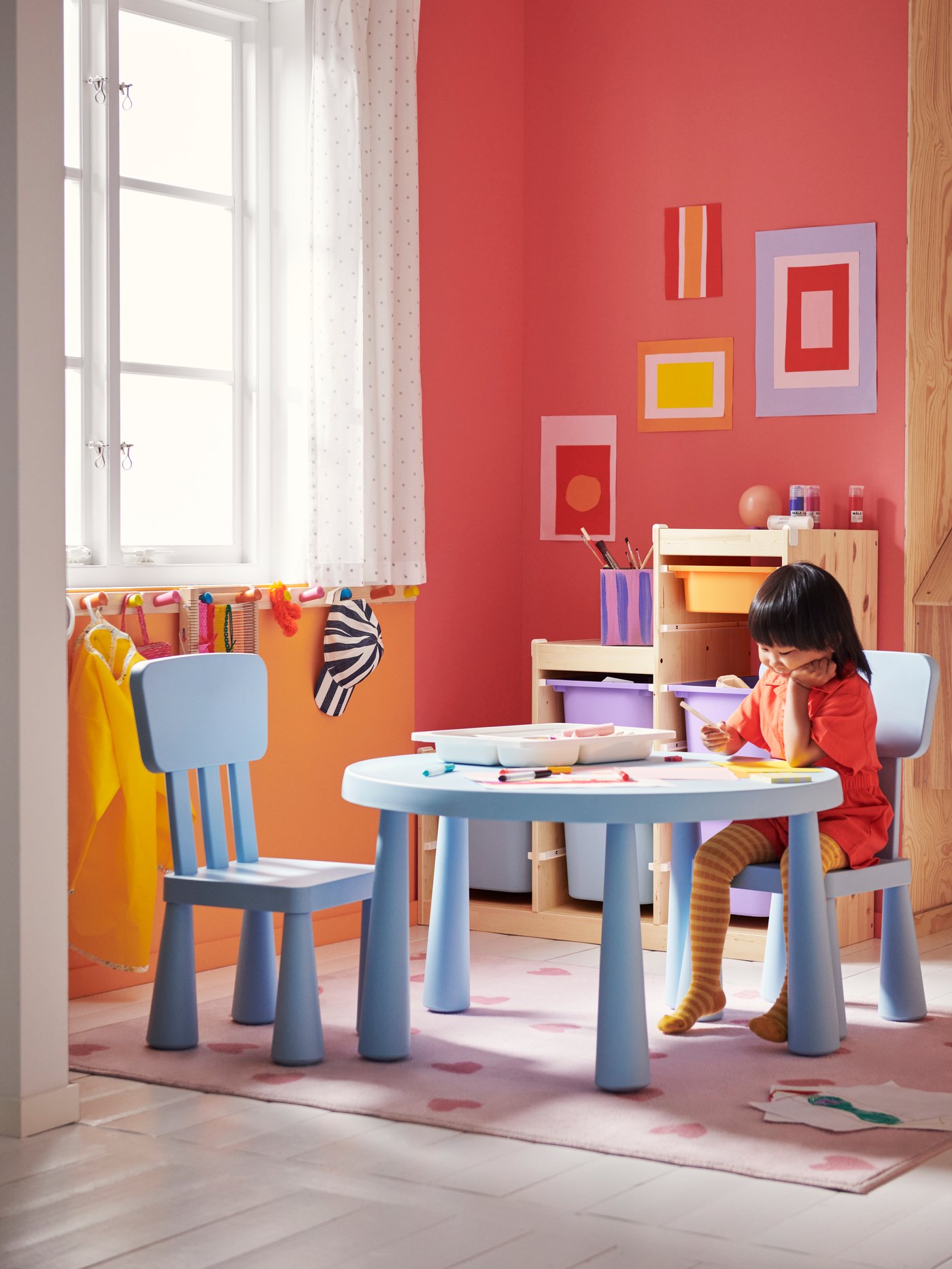 A child sitting on a MAMMUT chair at a MAMMUT children’s table drawing a picture. A tray of art materials is on the table.