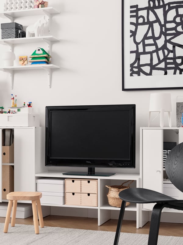 Bela TV stalaža, crni TV, uramljen crno-beli print, bele vitrine, ukrasni predmeti.